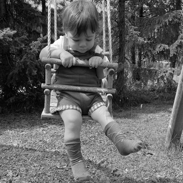 bambino in altalena in montagna con salopette di lusso e sostenibile made in italya