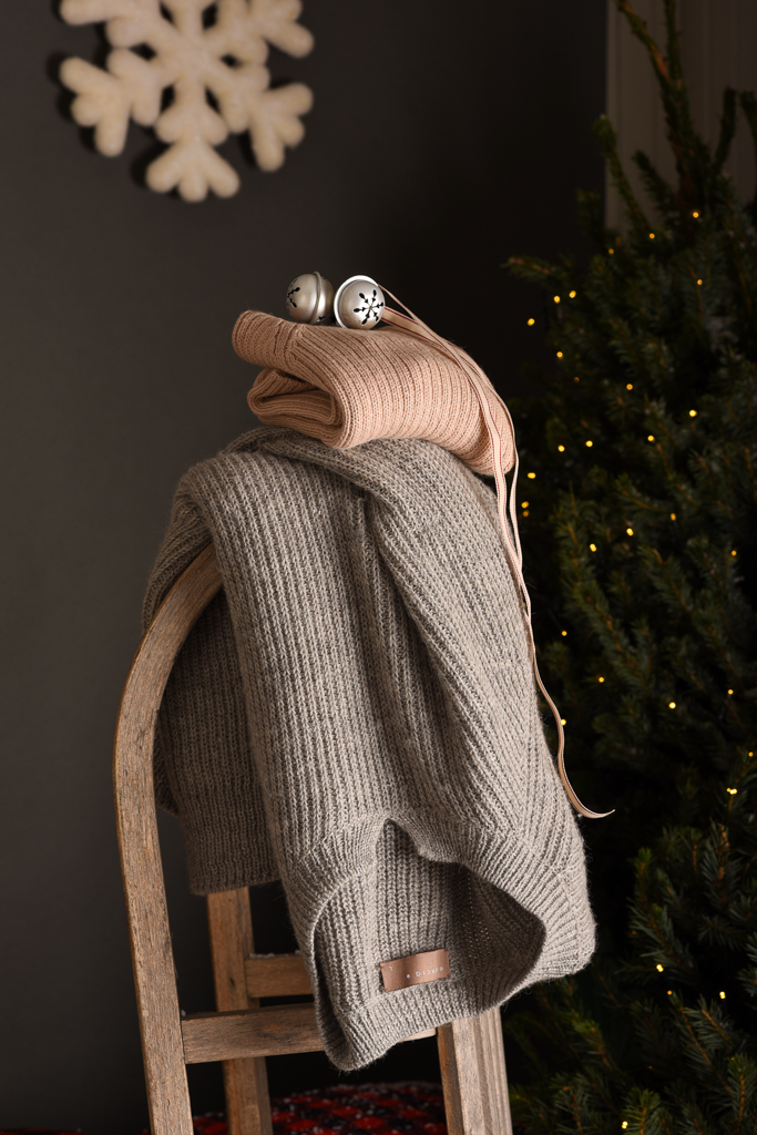 maglia calda per donna in pura alpaca realizzata eticamente appoggiata ad una slitta in un ambiente invernale